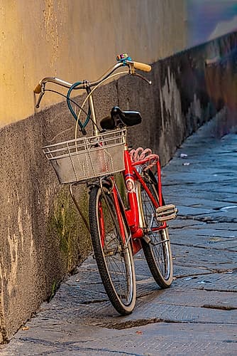 Red bicycle leaning against a wall in an alley. European Print